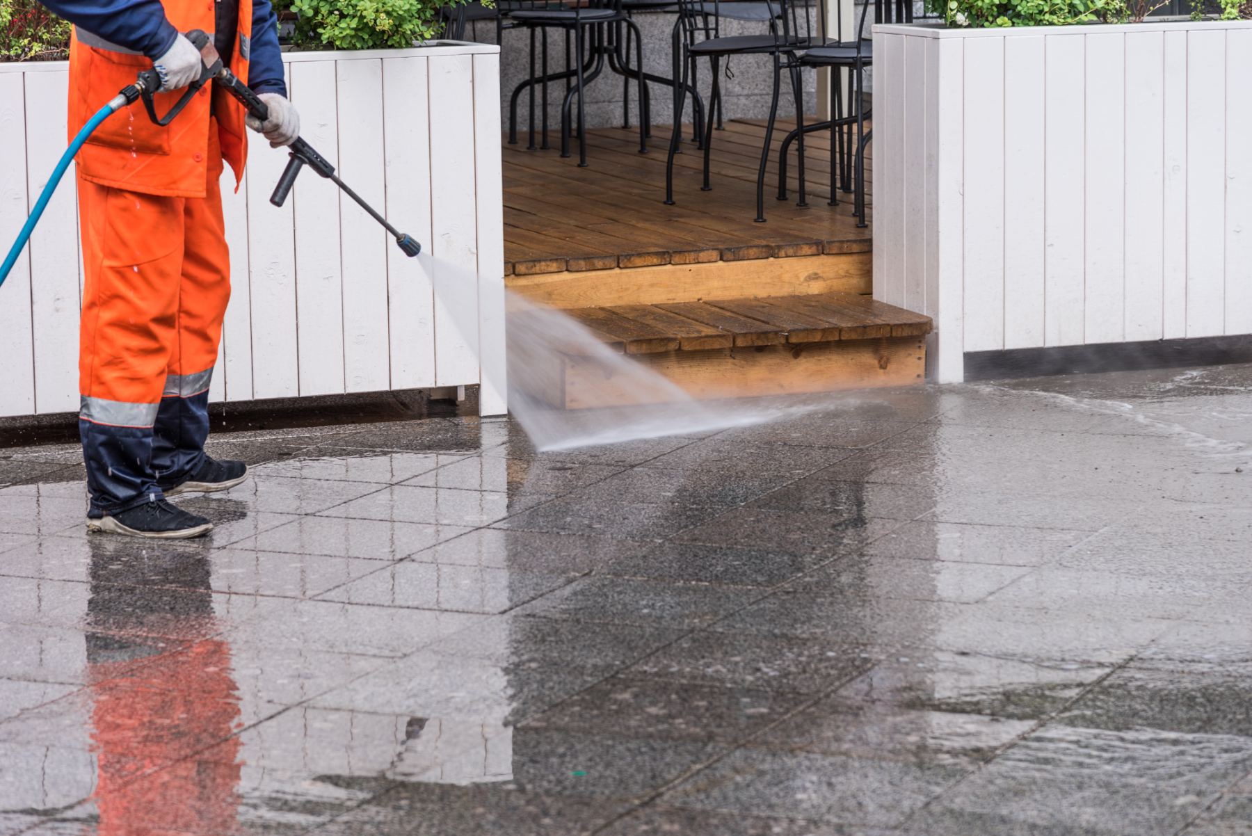 Worker in orange safety gear pressure washing wet pavement with hose