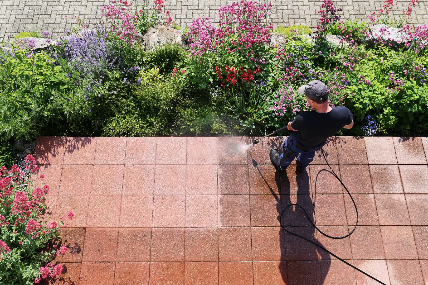 Worker pressure washing terracotta patio tiles surrounded by flowering plants