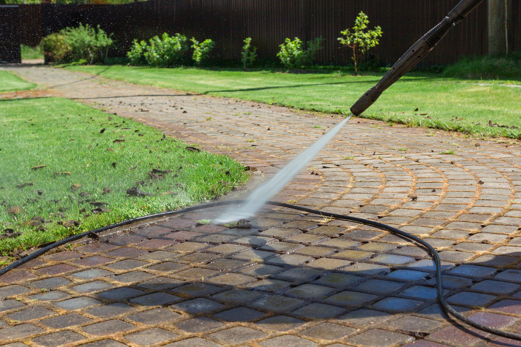 High-pressure washing cleaning brick patio with water stream and hose