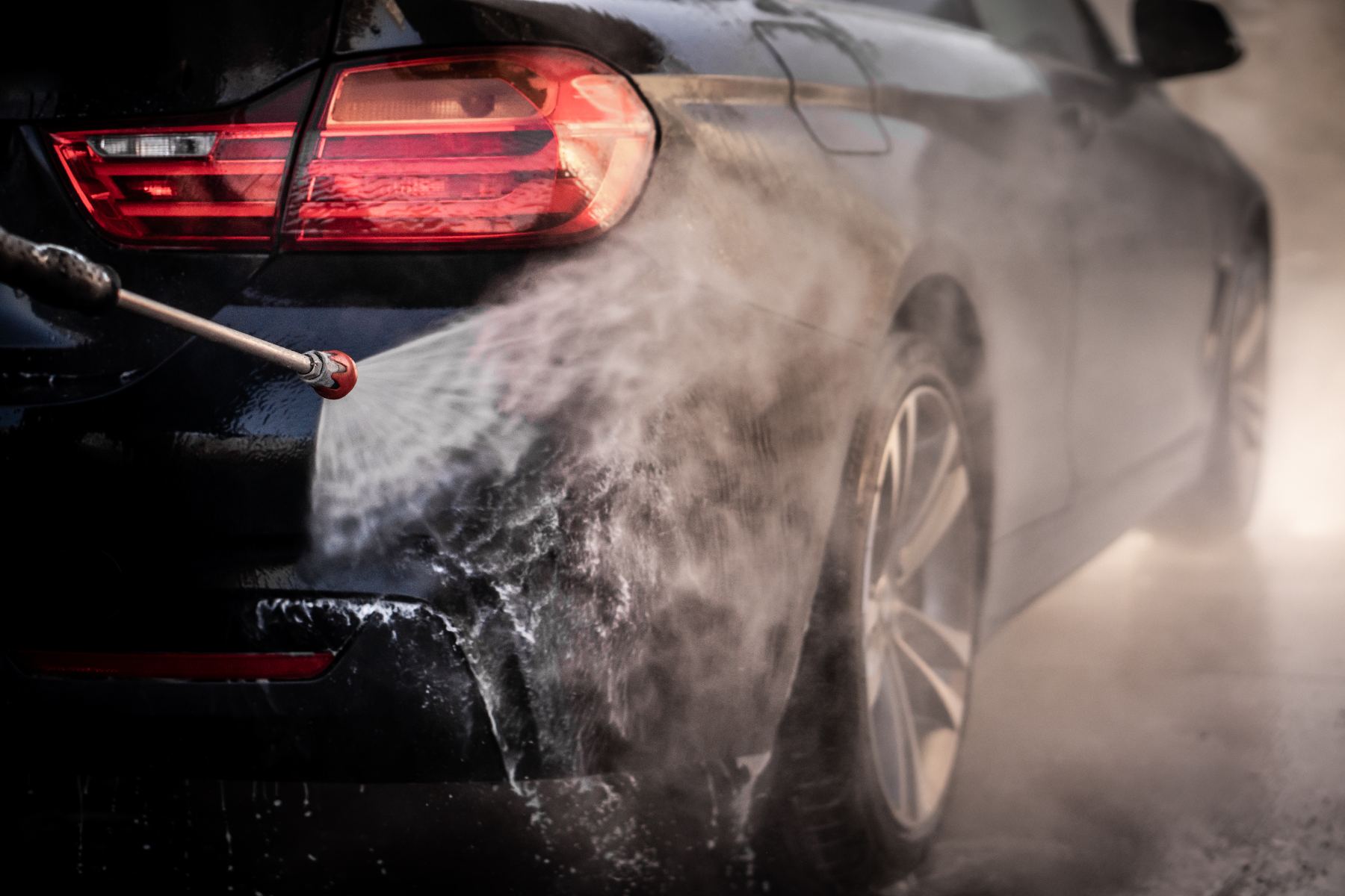 High-pressure water spray cleaning the side of a black car during professional washing service