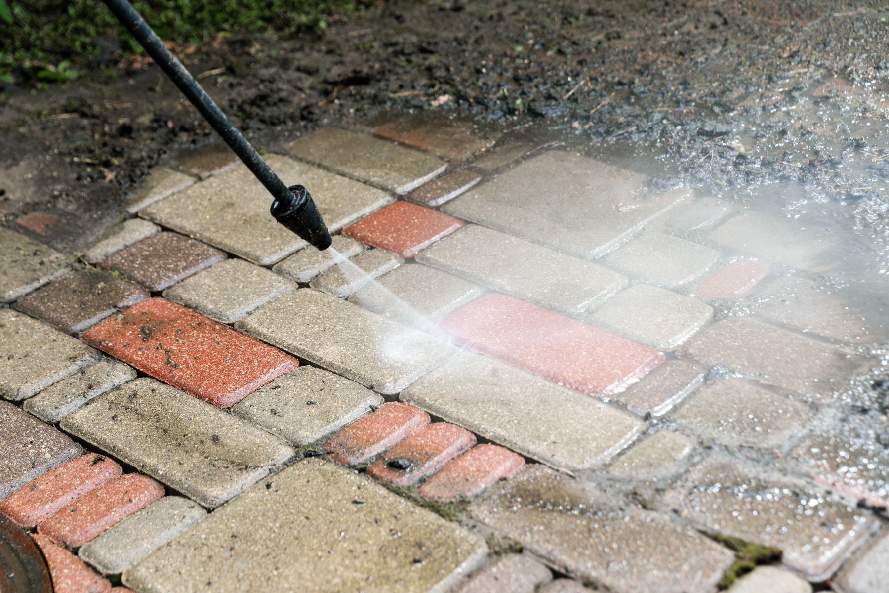 Pressure washing brick pavement with alternating red and tan colored bricks