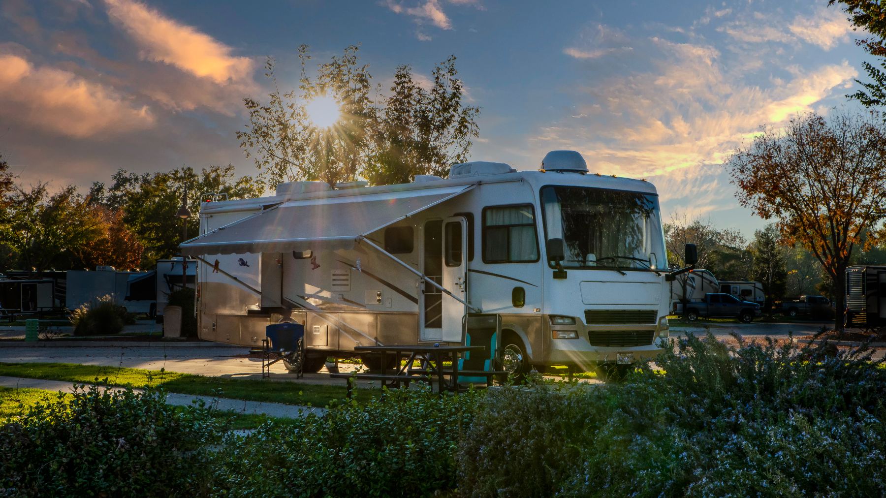 Modern Class A motorhome with extended awning parked at campground during sunset